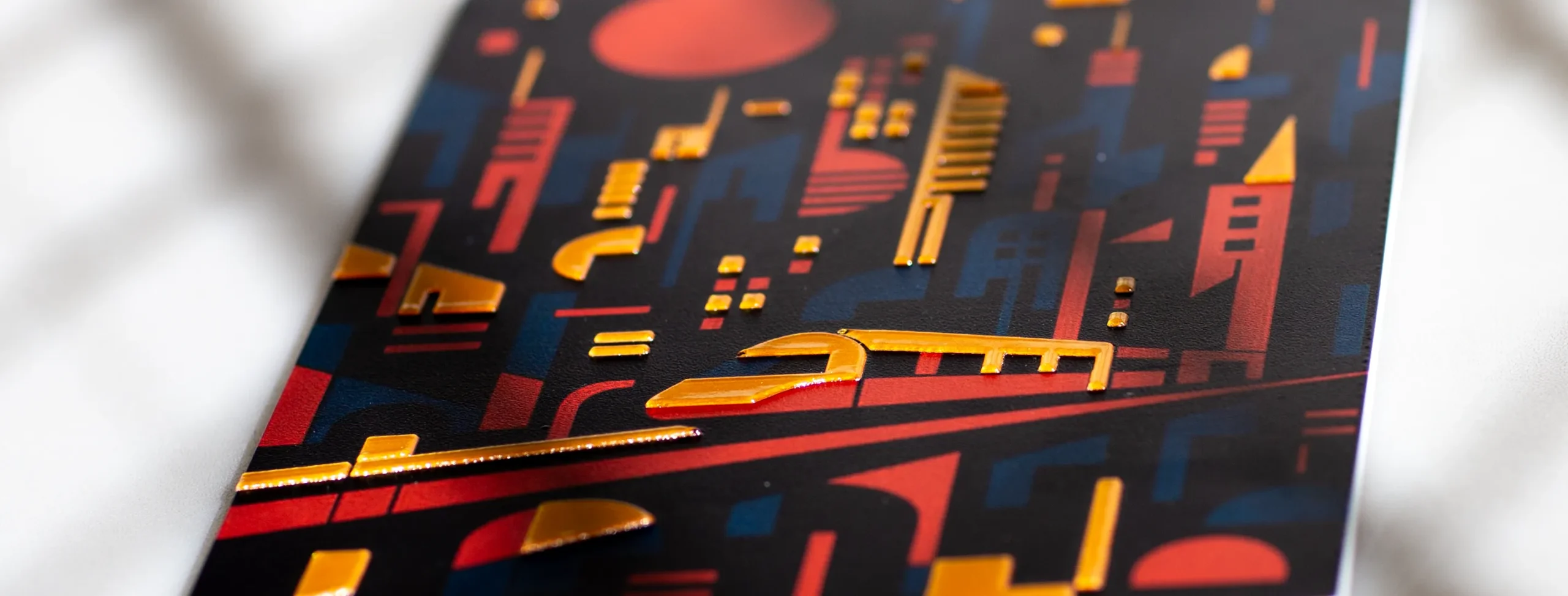 Close-up of gold foil UV printing on cityscape artwork with reflective raised gold details over red and dark blue print.