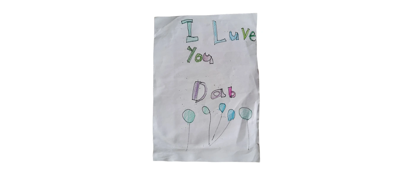 Child’s handwritten “I Love You Dad” note on white paper, decorated with colourful lettering and balloon-like drawings.