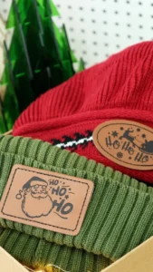 Green and red beanies fitted with engraved leather patches featuring festive designs.