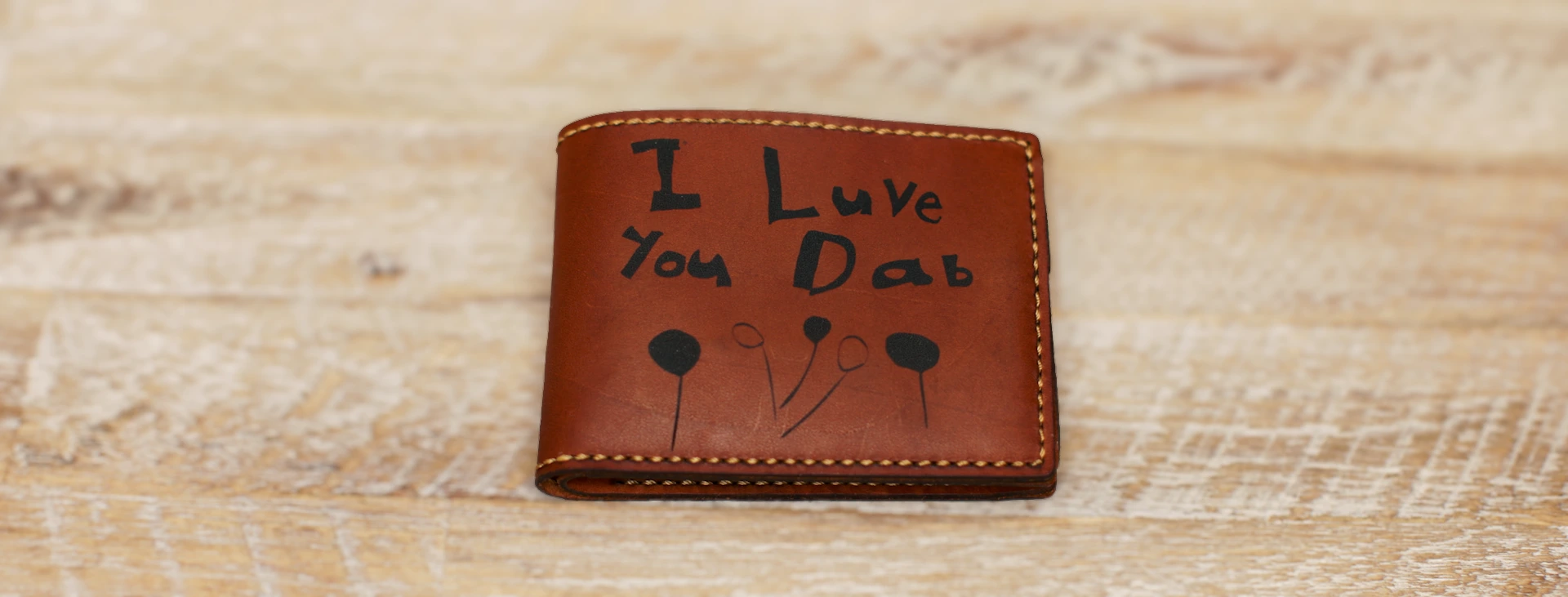 Finished leather wallet engraved with a child’s handwritten message and drawing.