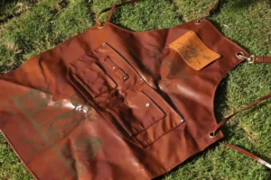 Brown leather work apron with engraved graphics, stitched tool pockets and an engraved leather patch.