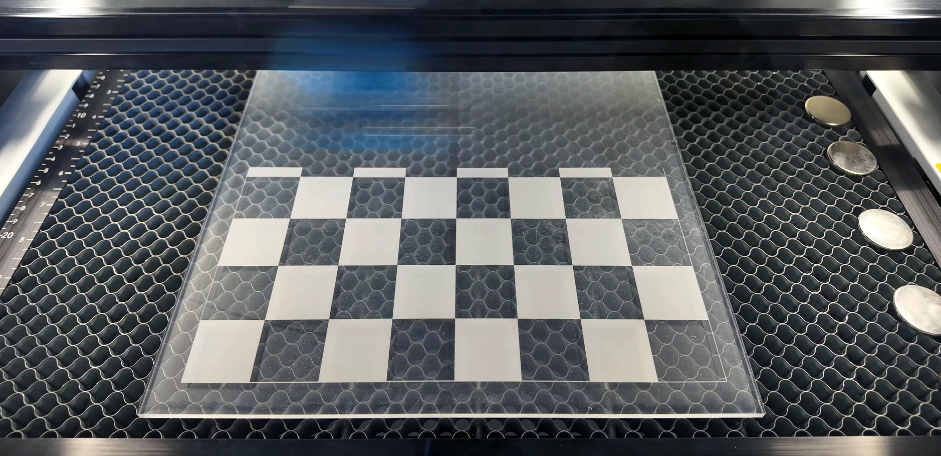 Clear acrylic checkers board with frosted squares positioned on a laser machine bed
