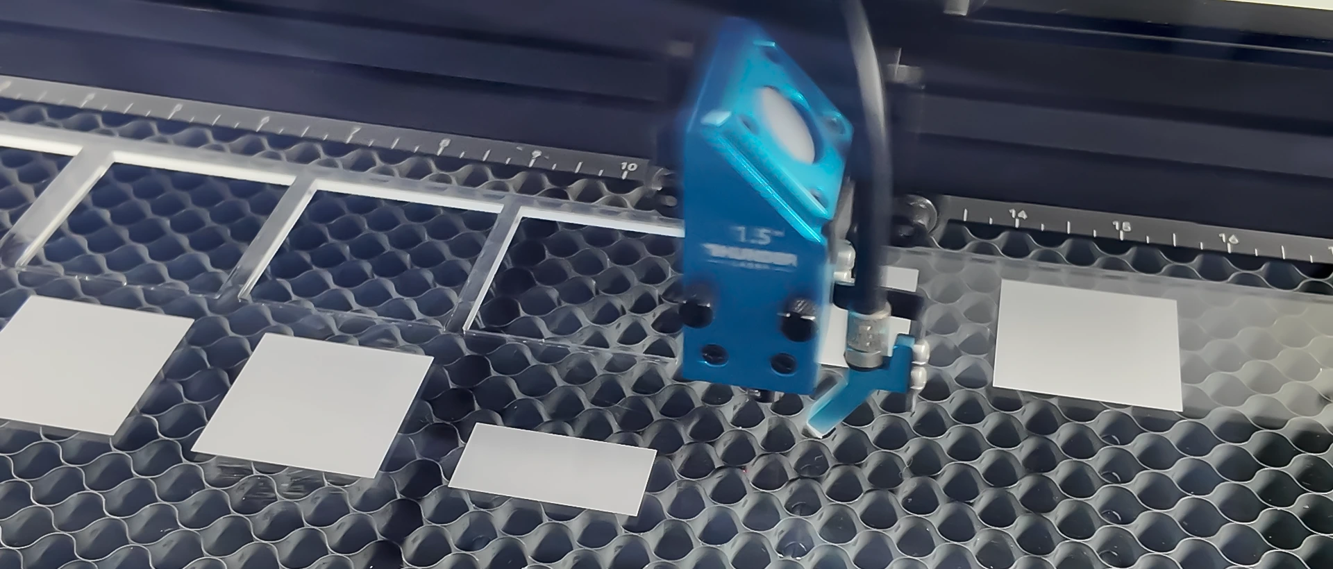 Laser head engraving frosted test blocks on a clear acrylic sheet