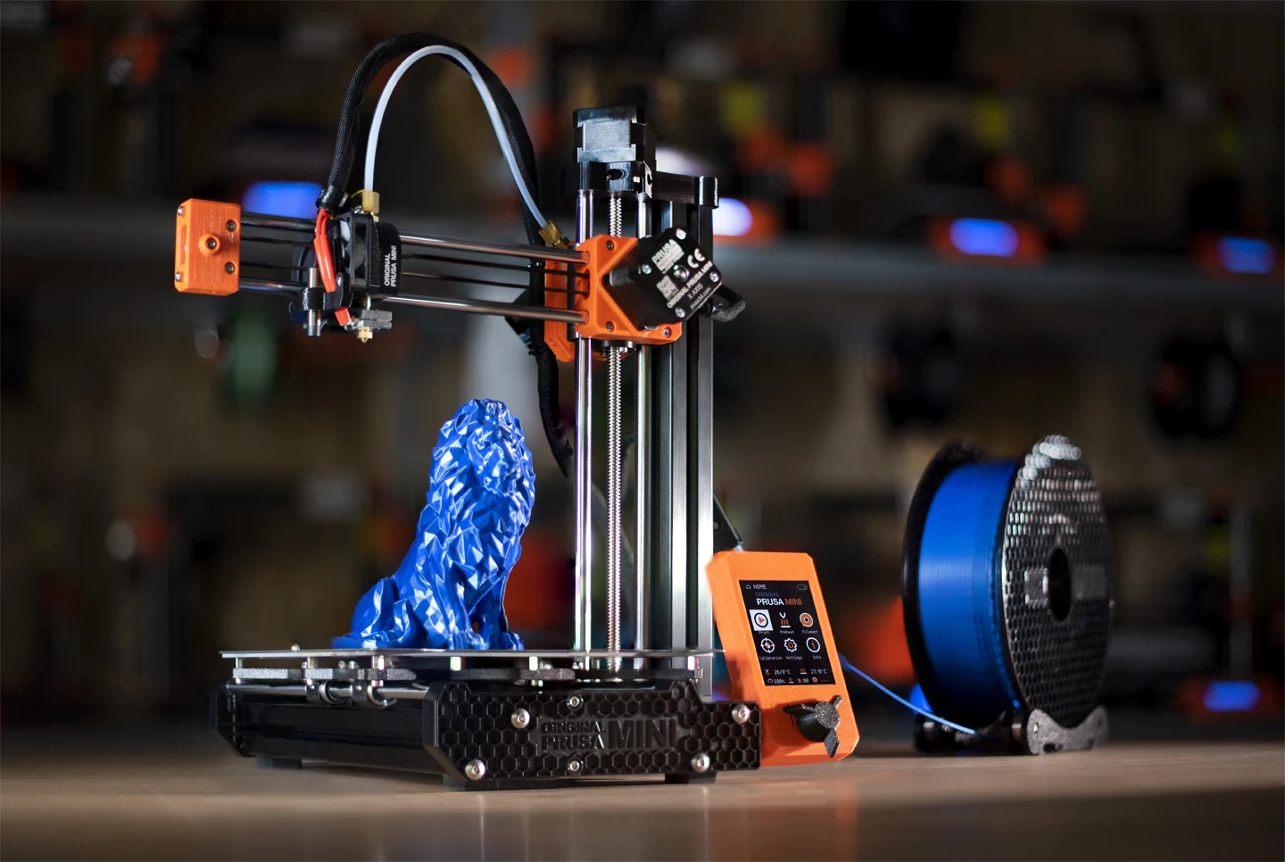 Original Prusa MINI+ FDM 3D printer producing a blue model using thermoplastic filament from a spool.